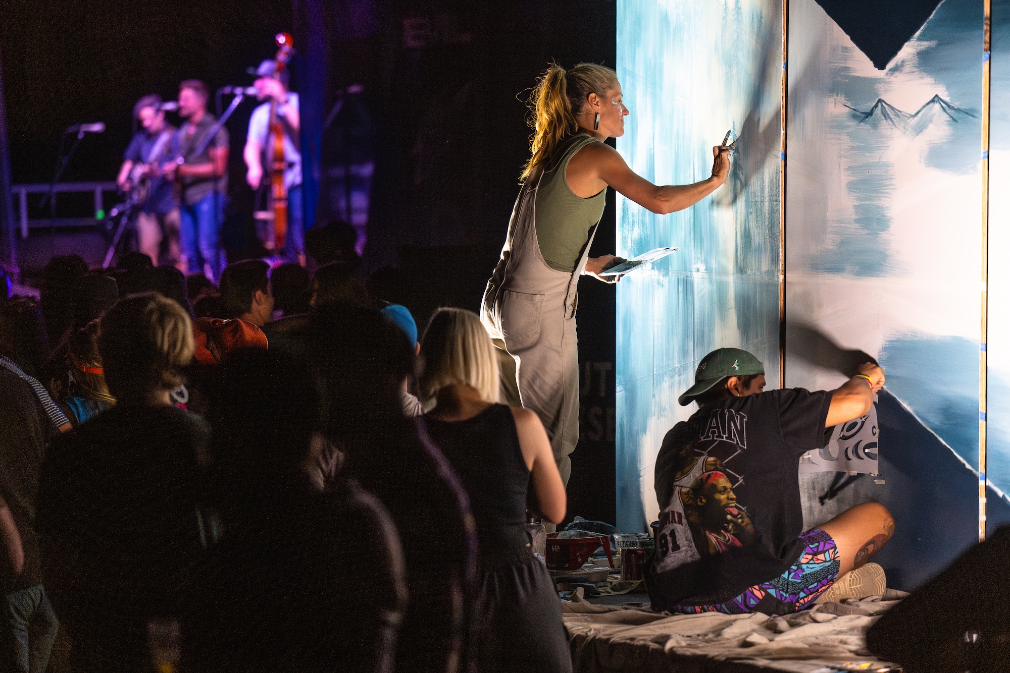 Two artists paint a mural alongside the main stage at NW Tune-Up